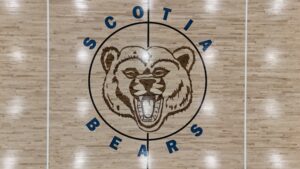 Basketball court floor with a large circular logo of a roaring bear's head, black outline, and blue lettering around the circle at center court.
