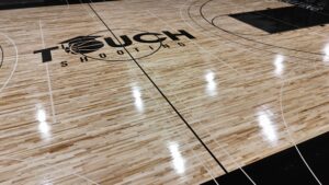 Basketball court floor with a large 'Touch Shooting' logo and court lines visible on polished wood surface, including a basketball graphic in the logo.