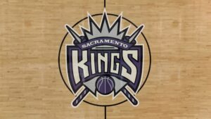 Sacramento Kings logo centered on a wooden basketball court floor at center court (team emblem in purple and white).