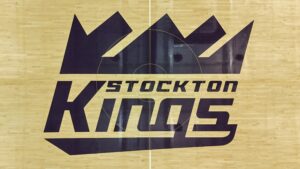 Large dark Stockton Kings logo on a light wooden gym floor with the word 'STOCKTON KINGS' beneath it