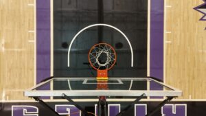 Basketball hoop centered on the backboard with an orange rim and white net on a gym court, viewed from above.