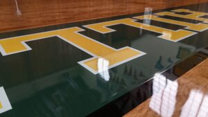 Close-up of a gym floor with large yellow block letters outlined in white on green surface.