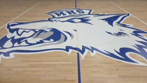Indoor basketball court with a large blue-and-white mascot logo spread across the center floor.