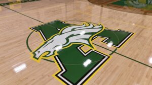 Wide shot of a polished gym floor featuring a large green and white mascot logo outlined in yellow at center court