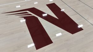 Large maroon stylized 'N' logo painted on a light wood gym floor in a sports court area.