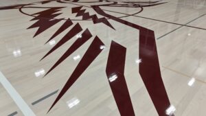 Maroon geometric sunburst logo painted on a light wooden basketball court floor.