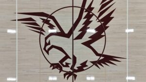 Large maroon circular abstract mural with jagged lightning bolt shapes on a light wood gym floor.