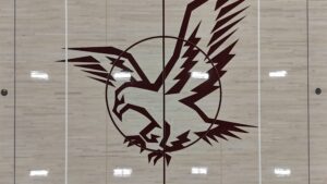Abstract maroon geometric design spanning multiple light wood gym panels; a circular motif with jagged angular shapes.