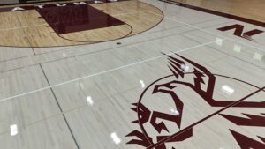 Polished gym floor with basketball court markings and a large maroon logo along the sideline.
