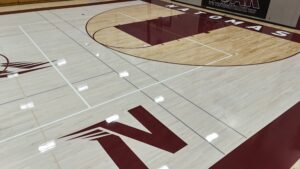 Indoor basketball court with light wood floor and maroon boundary lines, large 'NORTH' lettering along the sideline near the bottom left.