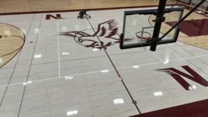 Overhead view of a gym basketball court; a person kneels and mops the polished floor near the center logo.