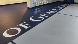 Indoor gym floor with a dark blue stripe along the length containing large white letters printed on the floor.