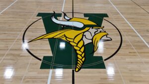 Gymnasium floor with a large school logo at center: a green shield behind a yellow and white bird mascot.