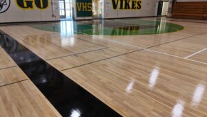 Indoor school gym with polished wooden floor, green center court area and 'GO VIKES' banners along the wall.