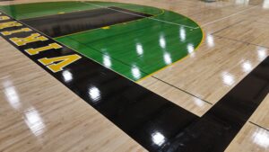 Indoor basketball court featuring a green painted key and black outer border with yellow boundary lines and lettering along the sideline.